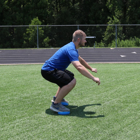 Balance Pod being used by both feet being stepped on while performing a squat to add an extra layer of difficulty.