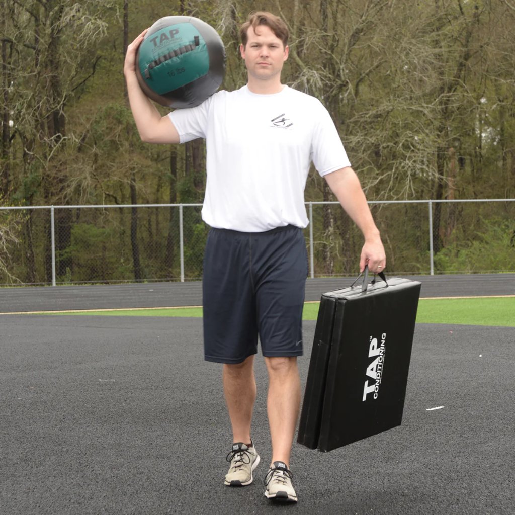 Athlete holding 16lb medicine ball overhead for baseball workout.