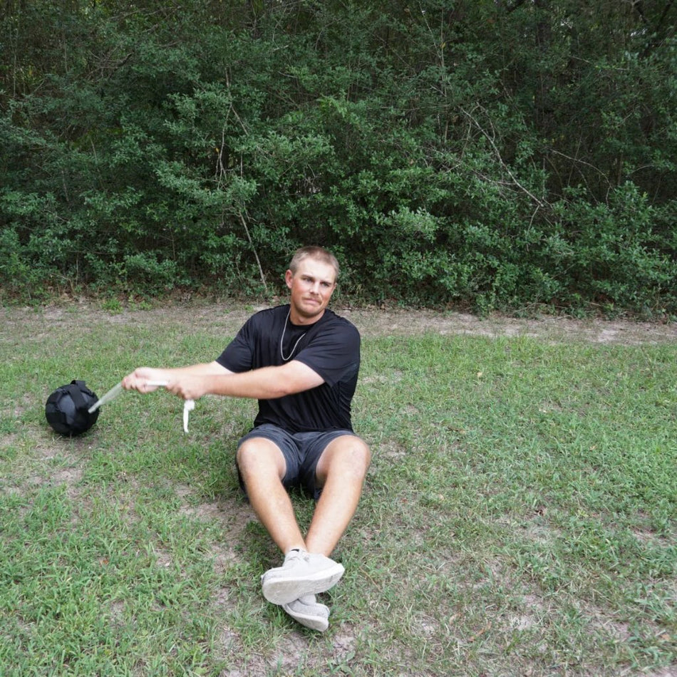 Person swinging Hammer Net SpeedBall while sitting on grass. Outdoor workout scene.