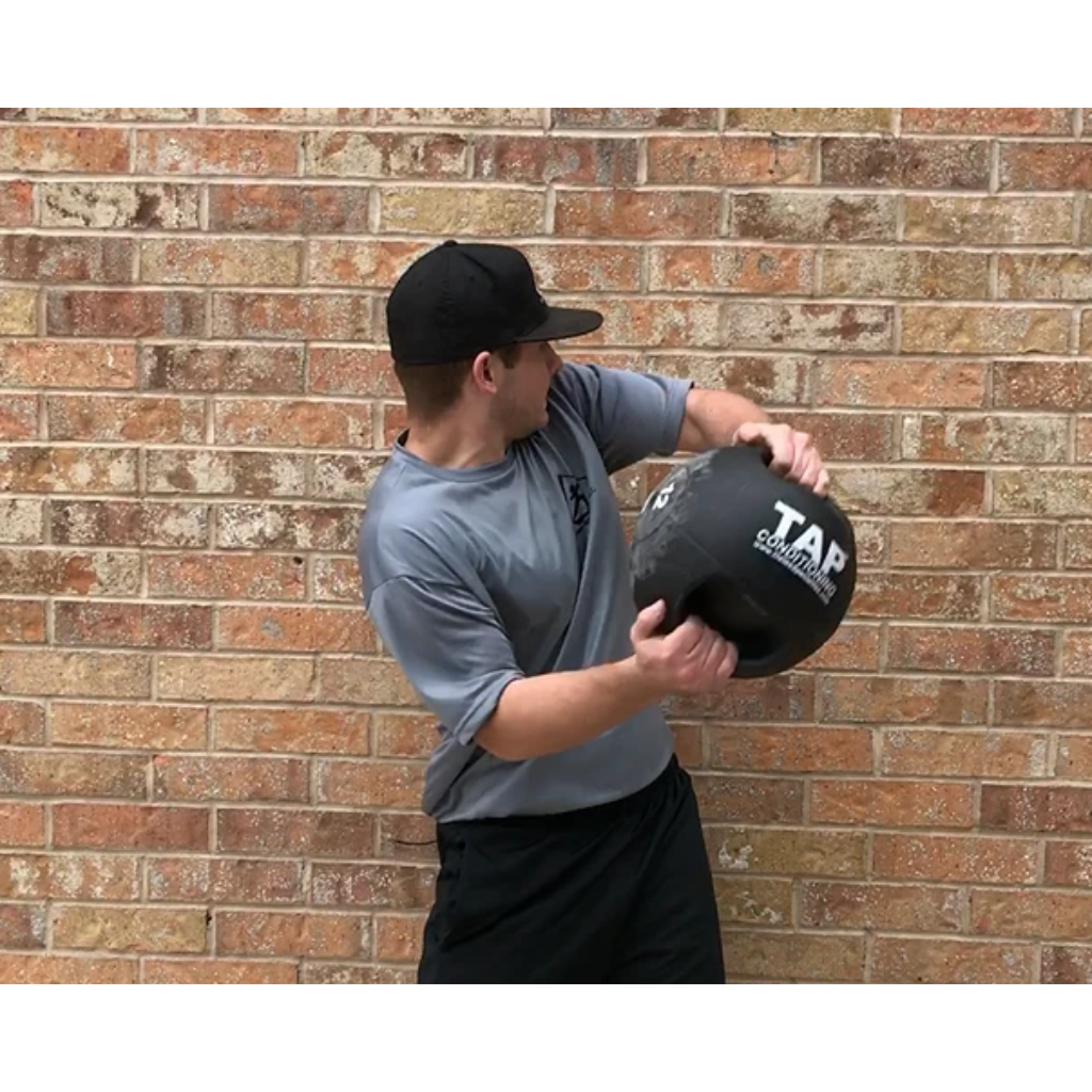 Athlete using a 12 lb Double Handle Medicine Ball against a brick wall—engaging in rotational strength training to enhance core power and functional movement.