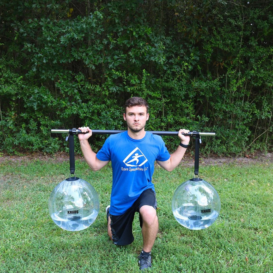 Athlete performing a lunge with the Khaos® Yoke, featuring two partially filled water balls suspended by straps from a bar, creating dynamic instability to engage core, knee, and hip stabilizers during functional training.